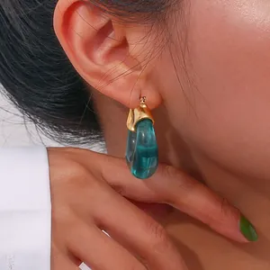 Detail view of U-shaped golden earring with green resin on model showing a modern retro style