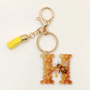 Close-up of letter H acrylic keychain with honey bee motif, yellow tassel, and lobster clasp