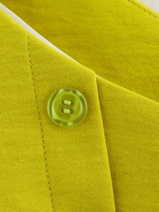 Dettaglio macro del tessuto twill verde lime con bottone in resina coordinato sul capo