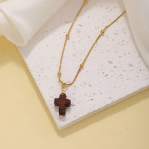 Detail of cross necklace with brown natural stone pendant on gold beaded chain