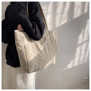 Large beige quilted nylon tote bag worn by a model in soft morning sunlight