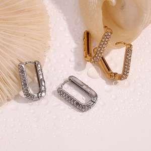 Close-up of gold and silver rectangular U-shaped earrings with rhinestones on wet surface