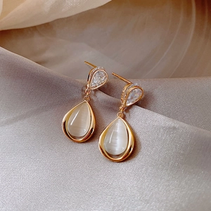 Close-up of teardrop opal earrings with zircon inlay on luxury grey silk background