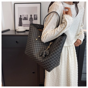 Detailed texture of charcoal grey tote bag featuring repeating M patterns and charm