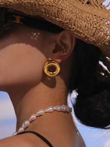 Detail of chunky gold hollow hoop earrings and a baroque pearl necklace on a model