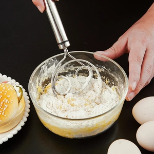 Action shot of manual stainless steel dough whisk mixing flour and egg in a glass bowl