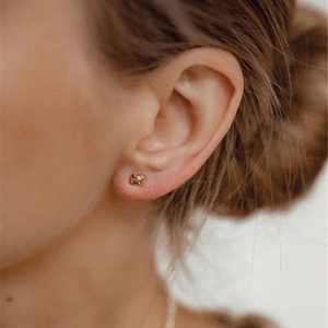 Close-up of a minimalist golden flower stud earring with diamond on woman's ear