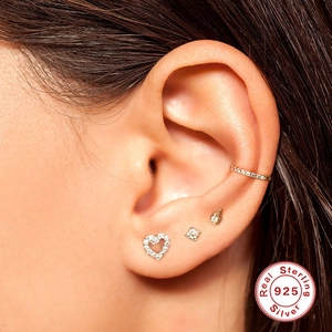 Macro shot of 925 sterling silver ear piercing set with heart and flower studs on ear