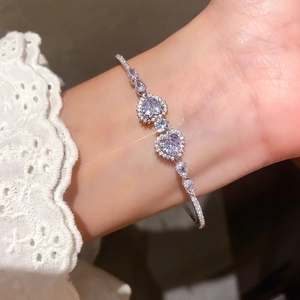 Detail of silver heart bracelet with purple zircons and white lace cuff on wrist