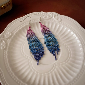 Detailed close-up of crystal feather earrings with pink and blue gradient rhinestones