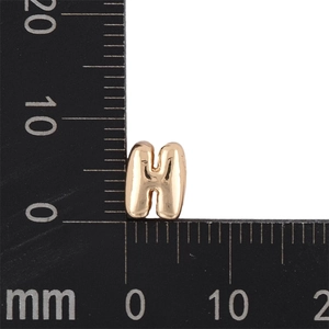 Close-up measurement of a golden bubble letter H charm with a millimeter ruler scale