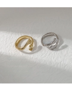 Detail of minimalist gold and silver palm-shaped hugging rings on white surface