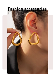 Detail of large gold teardrop twisted hoop earrings worn by a fashion model