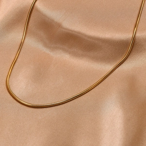 Macro shot of gold stainless steel snake chain necklace on beige silk fabric background