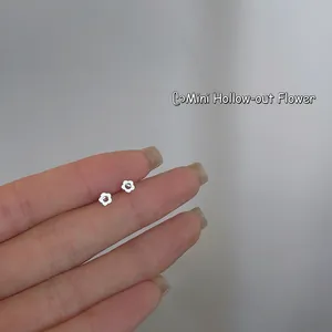 Close-up of minimalist 925 silver mini hollow flower stud earrings held by hand