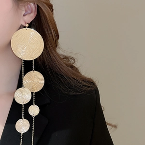 Detail of long gold tassel earrings with hammered metal circles worn by a model