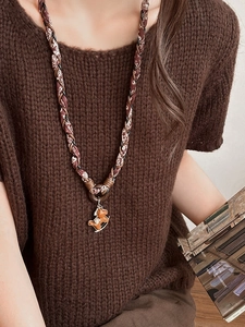 Détail d'un long collier tissé vintage avec pendentif cheval à bascule en bois sur un pull