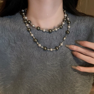 Détail d'un collier de perles double couche gris argenté sur l'encolure d'un pull gris