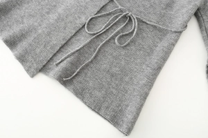 Dettaglio del cappotto grigio in maglia con trama del tessuto e cintura annodabile in vita