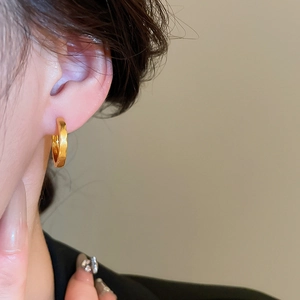 Close-up of gold hammered metal hoop earrings worn by a model in soft lighting