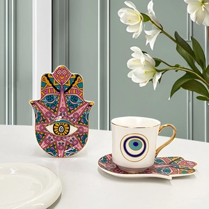 Detail view of ceramic coffee cup with Hamsa hand and Evil Eye patterns in a floral setting