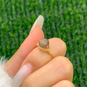 Macro detail of a handmade gold wire-wrapped ring featuring a grey opal gemstone bead