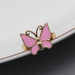 Macro shot of pink enamel butterfly ring on gold band leaning against white ceramic plate