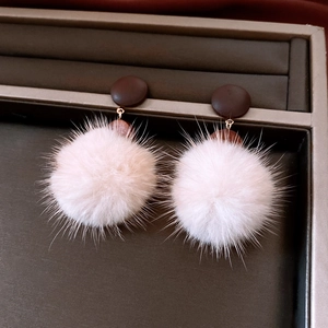Close-up of pink fluffy pom-pom earrings with dark brown round studs on a jewelry tray