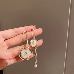 Close-up of asymmetric gold earrings with letter A pendant, rhinestones and pearls