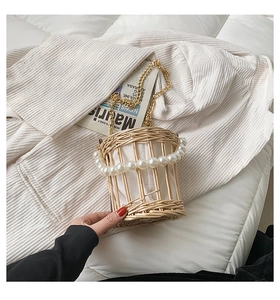 Detailed close-up of woven cage bag with pearl handle and metal chain on fabric