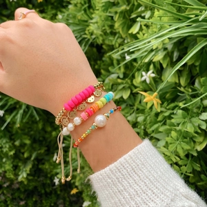 Close-up of stacked colorful clay beads and natural pearl bracelets on woman's wrist