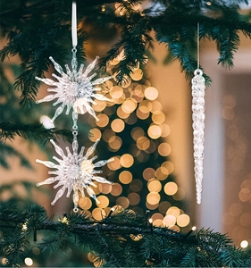 Close-up of transparent Christmas snowflake and icicle ornaments hanging on pine branches