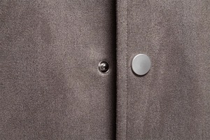 Détail macro du bouton-pression en métal argenté sur la veste en daim gris foncé
