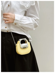 Detail of bright yellow mini crossbody bag with silver U-shaped metal handle and chain