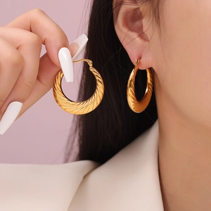 Twisted geometric gold hoop earrings in titanium steel shown on model with soft pink backdrop