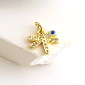 Macro shot of gold-plated dragonfly pendant with white zircon wings and blue evil eye detail