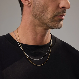 Detail of gold and silver snake bone chain necklaces worn together on a male model