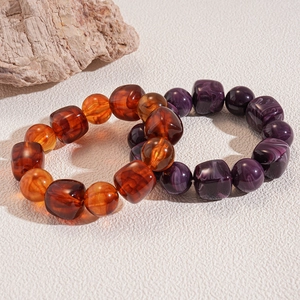 Macro shot of amber and purple textured acrylic beaded bracelets on a leather surface