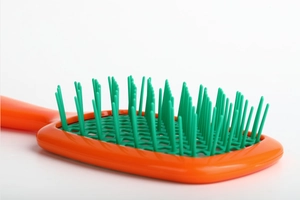Close-up of orange and green hollow honeycomb hairbrush with flexible plastic bristles