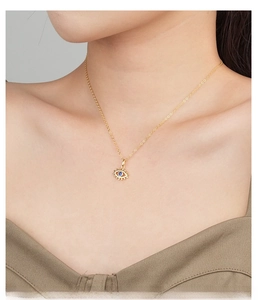 Close-up of a gold Evil Eye pendant with blue zircon on an O-chain worn by a model