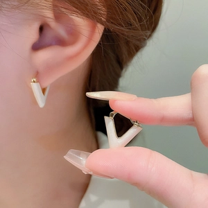 Detail of V-shaped gold earrings with pearlescent white inlay on ear and hand