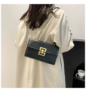 Detail of black matte leather square bag with gold geometric buckle and chain strap