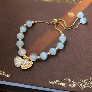 Détail du pendentif coquillage doré avec perle et perles oeil de chat sur un livre