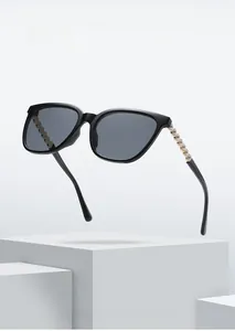 Detail of square black sunglasses featuring gold metal temples with elegant pearl accents