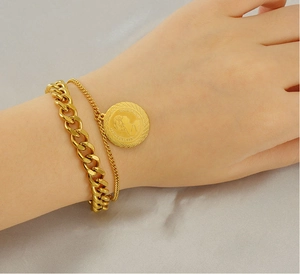 Detail shot of double-layered gold bracelet with a queen coin pendant on model wrist
