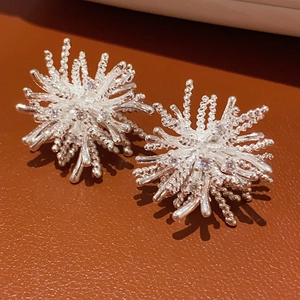 Detail of silver firework-shaped stud earrings with metallic pearls on leather background