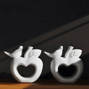 Artistic white ceramic apple ornaments with heart cutout and bird detail on wood