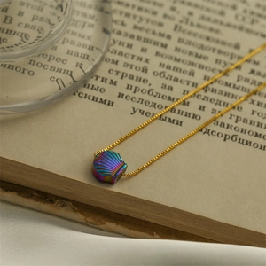 Golden box chain necklace with iridescent shell pendant placed on a vintage book