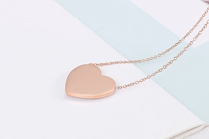 Detailed view of a polished rose gold heart pendant necklace on a clean blue background