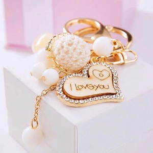 Detailed macro of golden heart keychain with I Love You engraving and white pom-pom